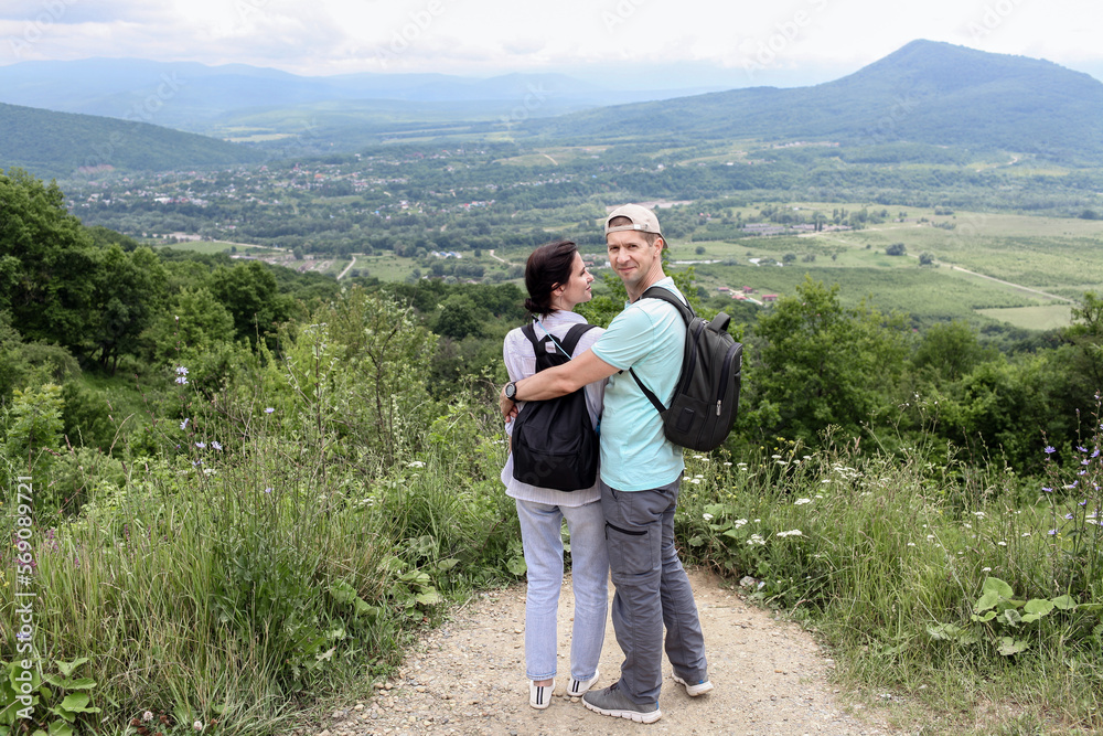 A man and a woman with backpacks stopped by the road in the summer and hugged, looking into the camera