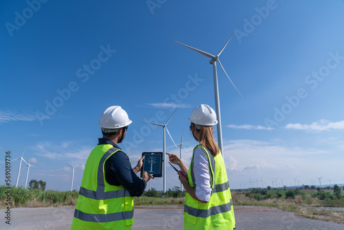 Engineer wearing uniform hold equipment box inspection work in wind turbine farms rotation to generate electricity energy. Green ecological power energy generation wind sustainable energy concept.