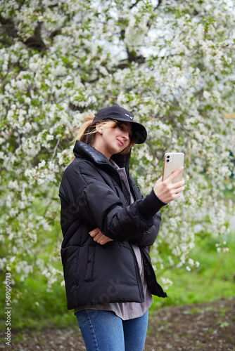 Young stylish millennial girl making a selfie under cherry blossom tree. Nature spring, connecting with nature, self-discovery lifestyle