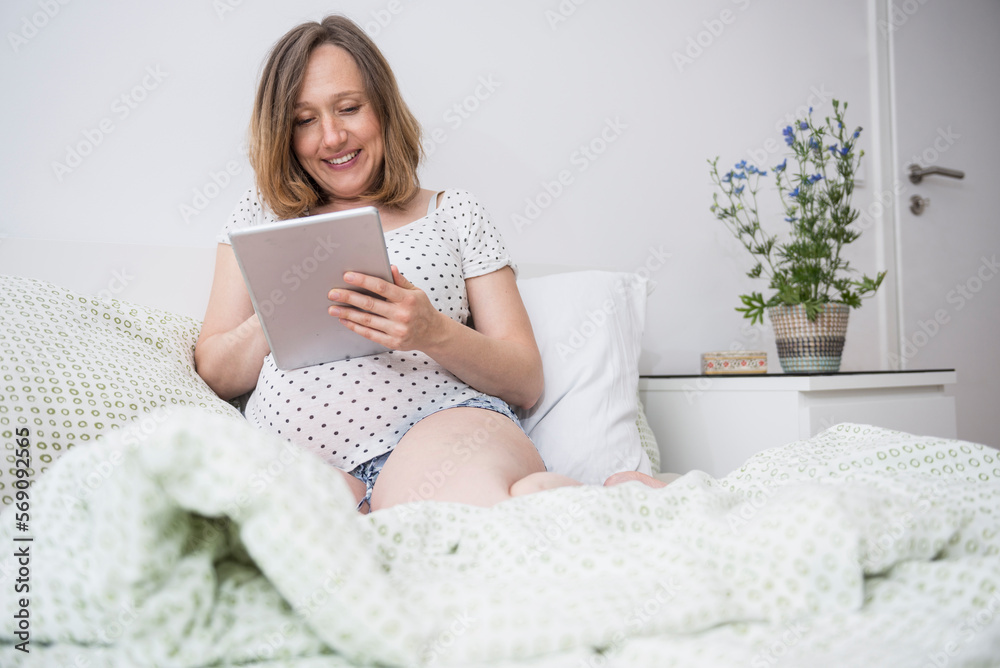 Happy pregnant woman using digital tablet in bed, Munich, Bavaria, Germany Happy pregnant woman using digital tablet in bed, Munich, Bavaria, Germany