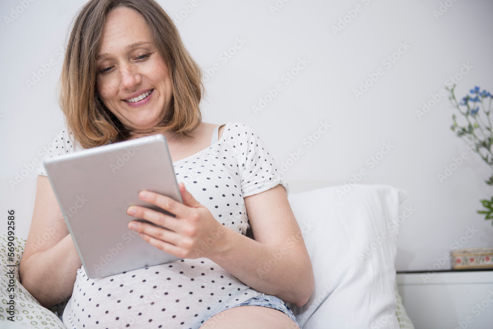 Happy pregnant woman using digital tablet in bed, Munich, Bavaria, Germany Happy pregnant woman using digital tablet in bed, Munich, Bavaria, Germany
