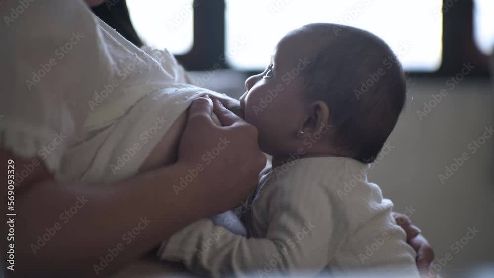 Bebé sentado sonriendo en posición de caballito comiendo de pecho de mamá sentada en sofá amamantado.