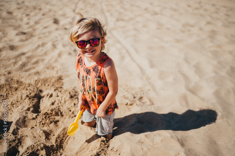 Happy young boy wearing sunglasses at beach playing with shovel Happy young boy wearing sunglasses at beach playing with shovel