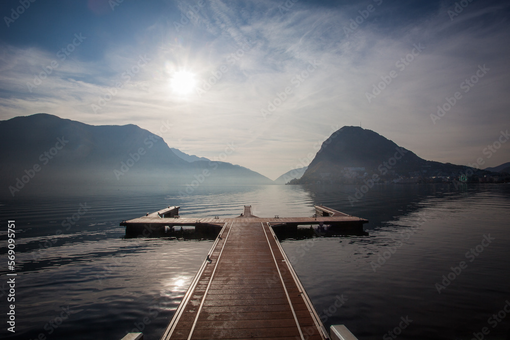 Obraz premium Autumnal dramatic down from mooring in the Lugano lakefront with San Salvatore peak and Italian mountains in the background, Switzerland. Concept about serenity and relaxation