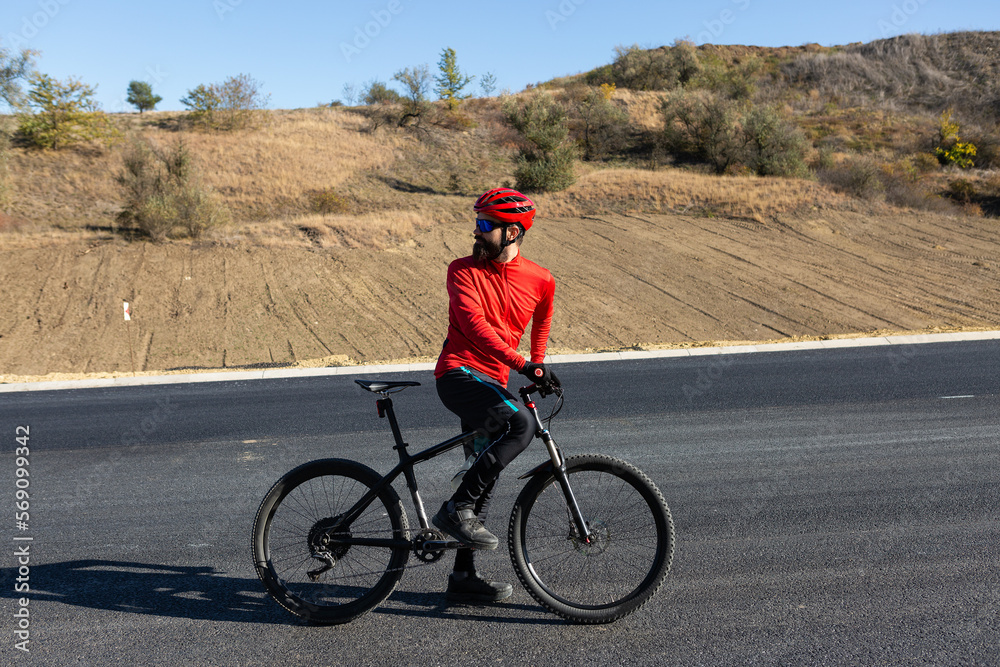 Cyclist riding bicycle on road against clear sky. A man in an outfit stands with a bicycle on an autumn sunny day.