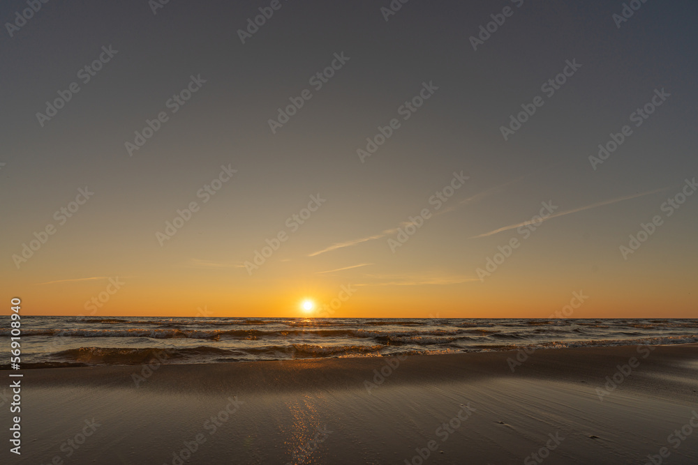 Sunset in a cloudless sky on the coast of the Gulf of Finland in Ust-Narva. The sky is clear, the waves gently roll on the sand. Estonia, Narva-Jyesuu. Natural background. Space for text.