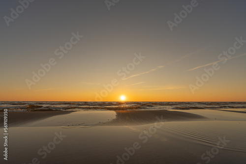 Sunset in a cloudless sky on the coast of the Gulf of Finland in Ust-Narva. The sky is clear, the waves gently roll on the sand. Estonia, Narva-Jyesuu. Natural background. Space for text.