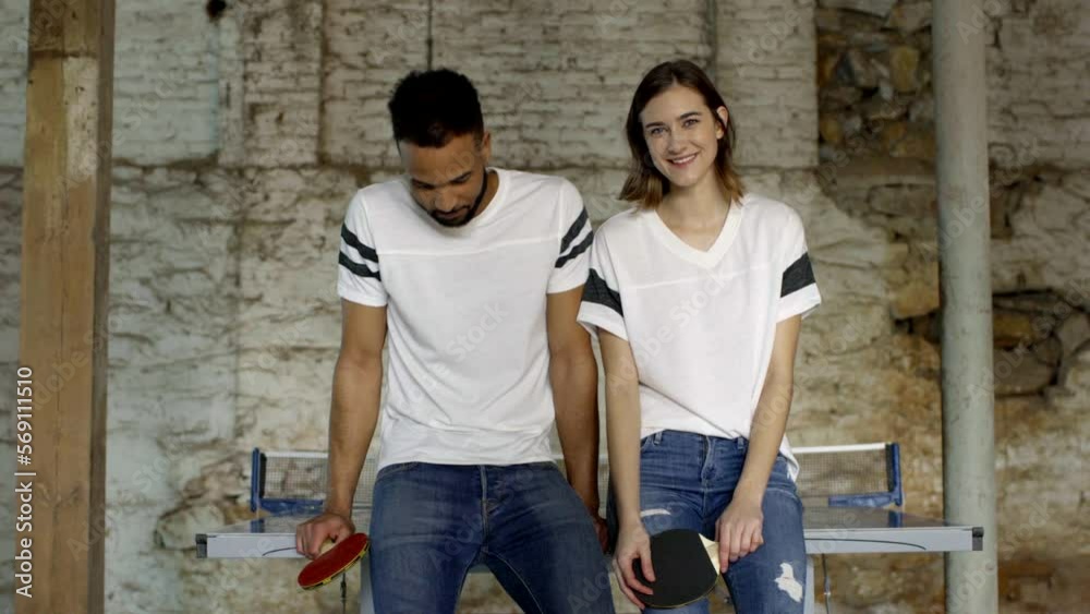 Dolly shot of smiling young couple holding table tennis rackets against wall in old building