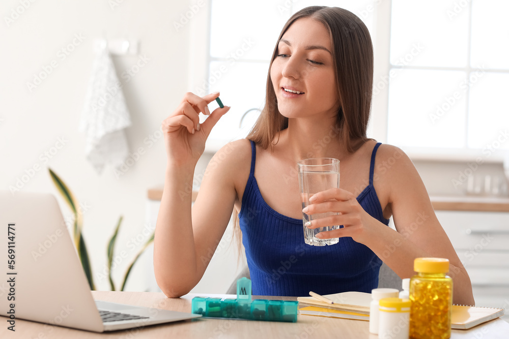Beautiful woman with glass of water taking vitamin supplement in kitchen Beautiful woman with glass of water taking vitamin supplement in kitchen