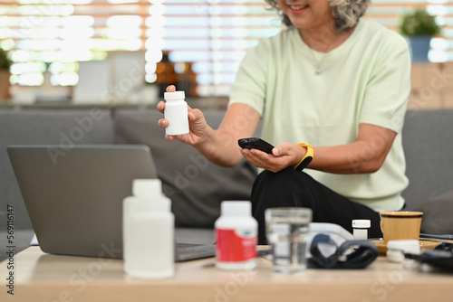 Mature woman holding pills bottle, discussing prescription medications with doctor on video call. Telehealth consultation concept