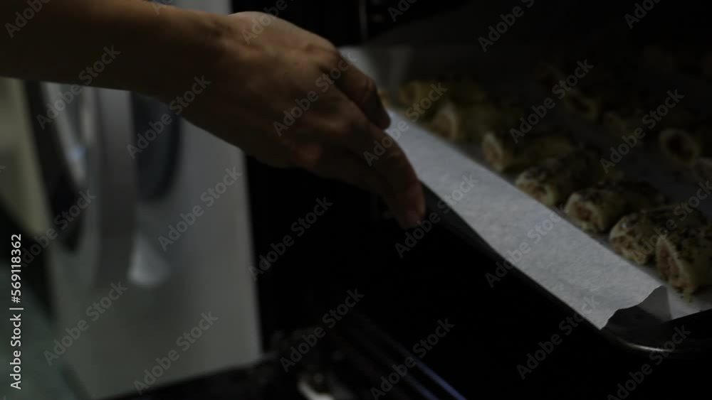 Person putting tray with rolls in hot oven during pastry preparation Person putting tray with rolls in hot oven during pastry preparation