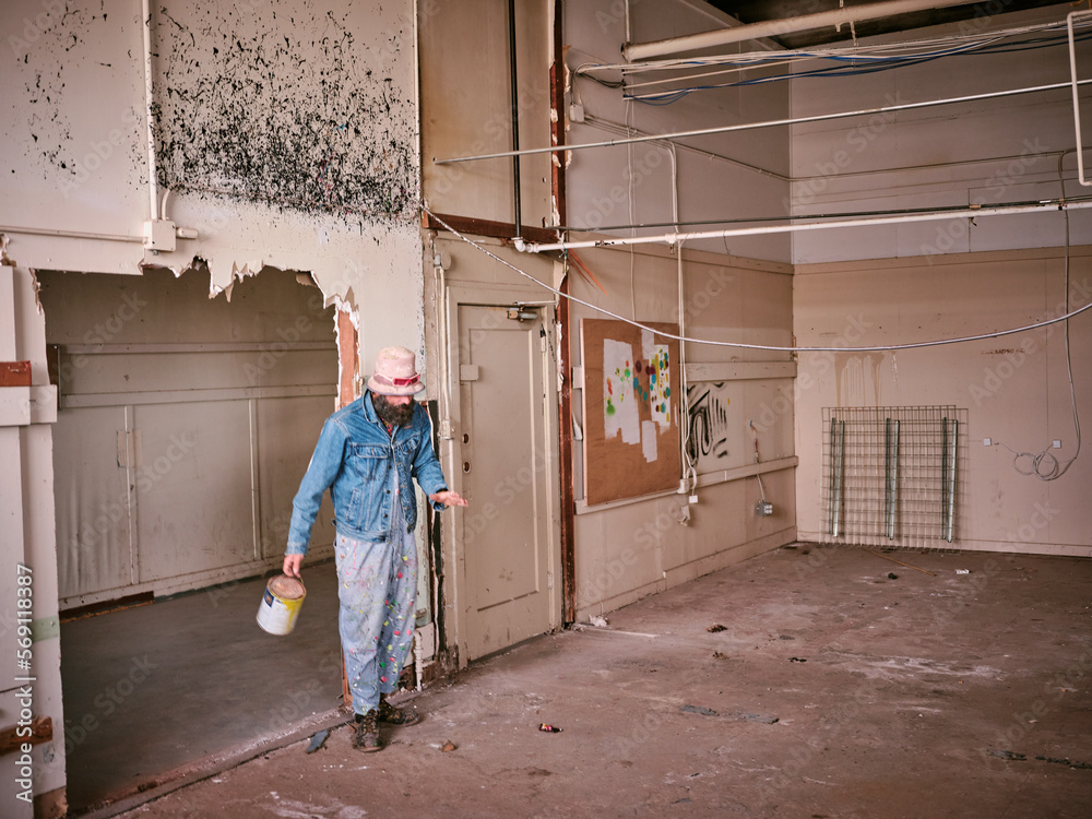 Man sands with can of paint in a falling apart and abandoned space.