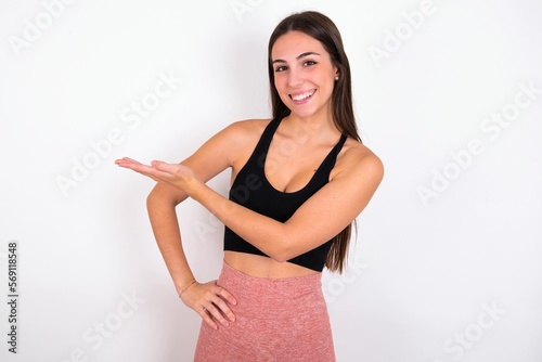 young woman wearing sportswear over white studio background says  wow how exciting it is  has amazed expression  shows something on blank space with palm. Advertisement concept.