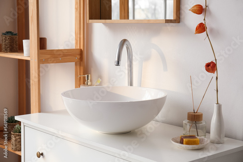 Ceramic sink  vase with plant branch and bath accessories on drawers in bathroom