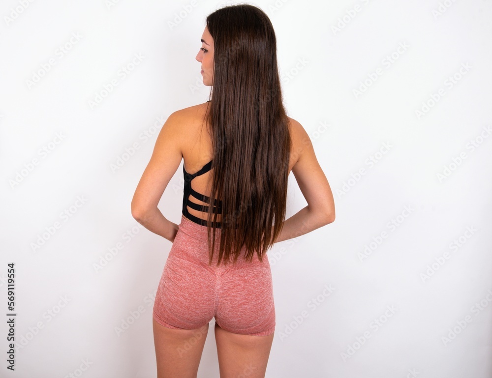 Naklejka premium The back view of young woman wearing sportswear over white studio background Studio Shoot.