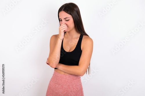 young woman wearing sportswear over white studio background, holding his nose because of a bad smell.