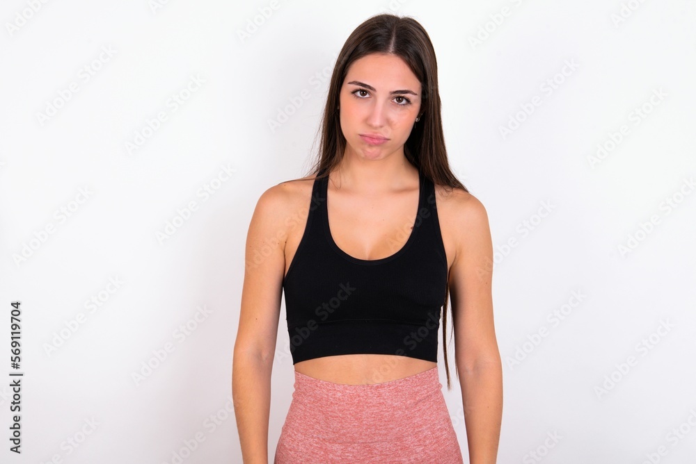 Gloomy, bored young woman wearing sportswear over white studio background frowns face looking up, being upset with so much talking hands down, feels tired and wants to leave. Gloomy, bored young woman wearing sportswear over white studio background frowns face looking up, being upset with so much talking hands down, feels tired and wants to leave.