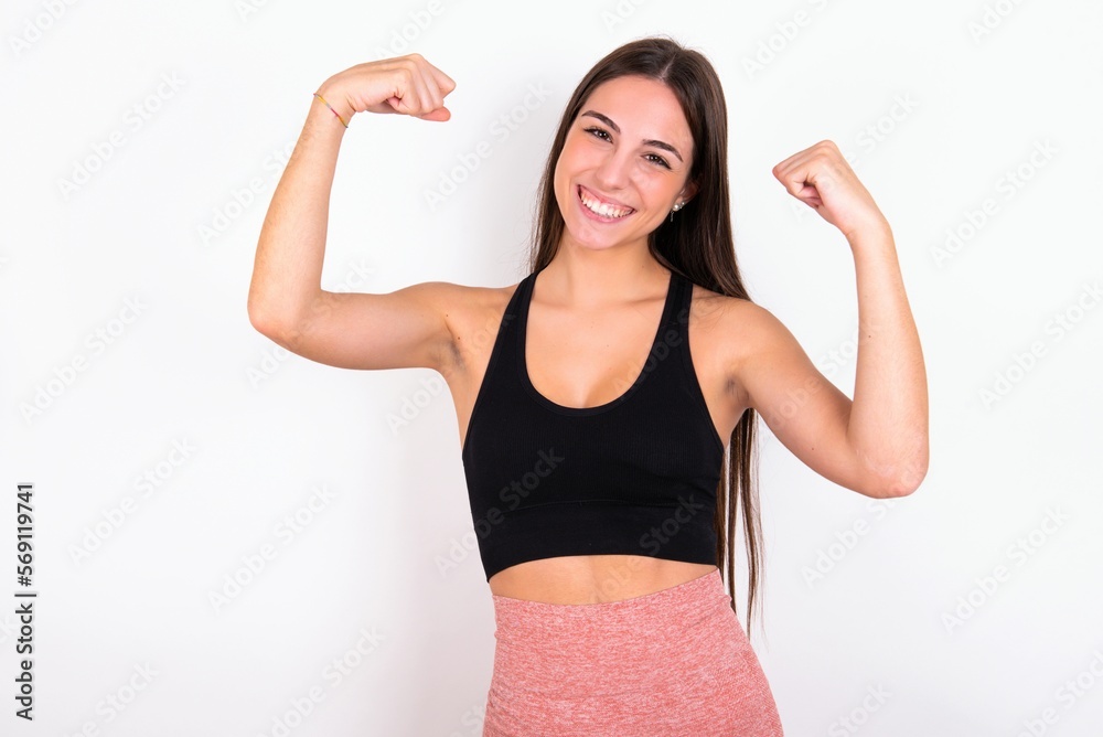 Yes I am winner. Portrait of charming delighted and excited young woman wearing sportswear over white studio, raising up fist in triumph and victory smiling achieving success grinning from delight. Yes I am winner. Portrait of charming delighted and excited young woman wearing sportswear over white studio, raising up fist in triumph and victory smiling achieving success grinning from delight.