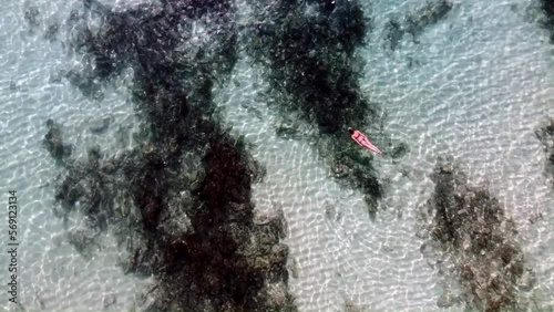 Drone shot of turquoise clear water with dark algae or rock formations and a small pink kayak floating. Concept of nature, adventure, exploration, marine environment, and aerial photography.