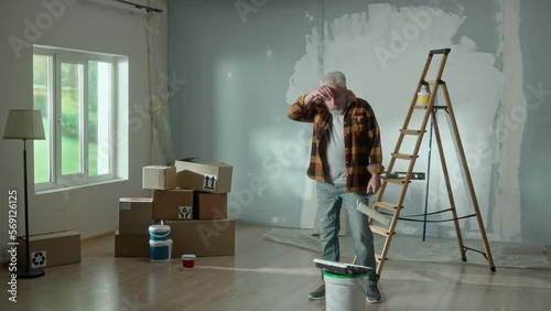 Tired grandpa entering the room and grandson merrily jumping out from behind stack of cardboard boxes. Young teenager is scaring an older man and together they laugh merrily at a joke. photo