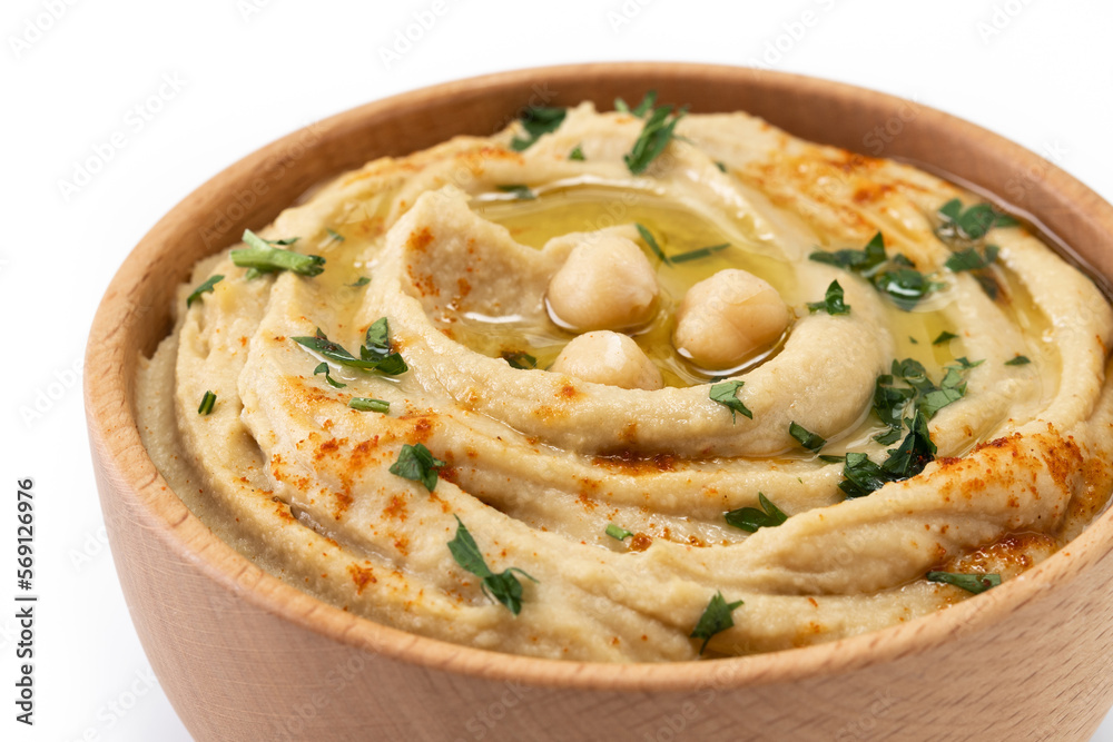 Chickpea hummus in a wooden bowl garnished with parsley, paprika and olive oil isolated on white background. Close up
