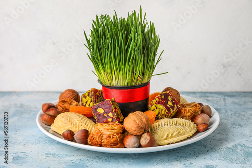 Plate with treats and grass on table near white wall. Novruz Bayram celebration photo