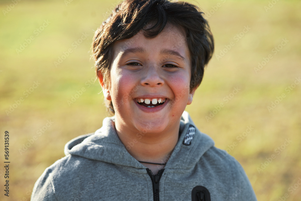 Happy, smile and portrait of a child in nature having fun while enjoying outdoor fresh air. Happiness, excited and face of a boy kid standing in a park while on a summer vacation, holiday or trip.