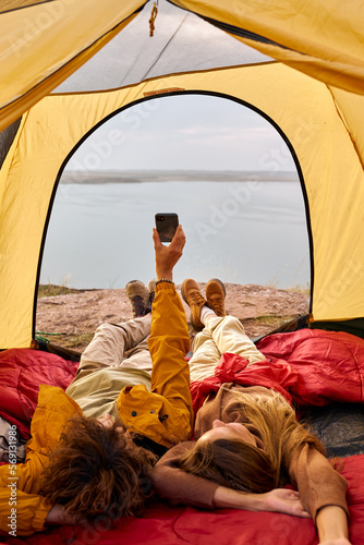 couple relaxing in camper tent and enjoying mountain autumn lake views. Cozy early autumn couple hiking traveling concept image. young caucasian relaxed male and female having rest