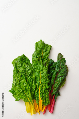 Bunch of rainbow swiss chard leaves on beige stone table. Top view of yellow, orange, red and green fresh swiss chards.