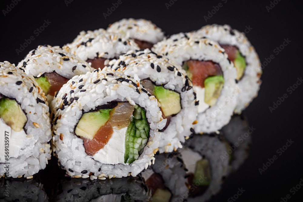 sushi roll with sesame avocado cucumber tuna and Philadelphia cheese on a black mirror background sushi roll with sesame avocado cucumber tuna and Philadelphia cheese on a black mirror background