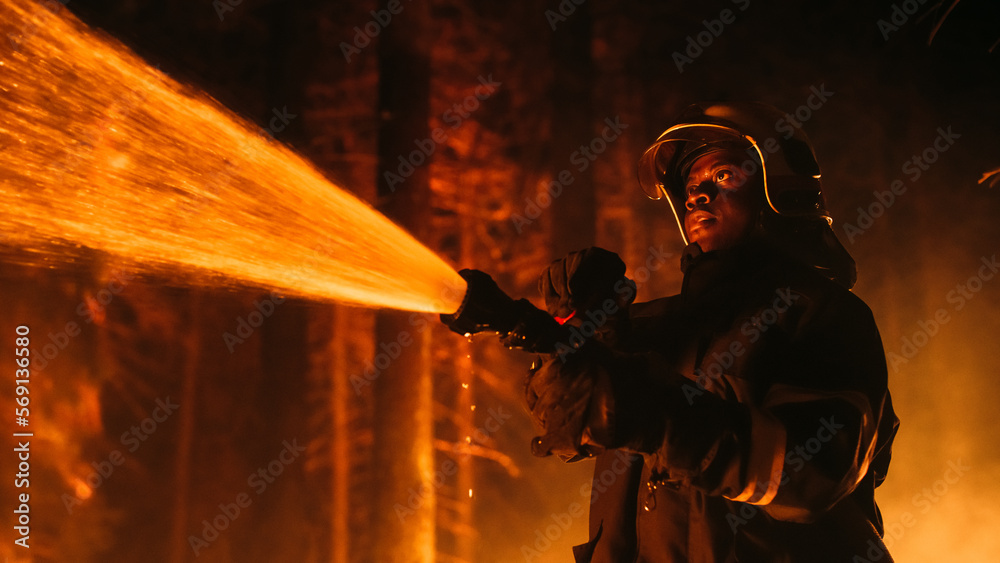Close Up Low Angle Creative Portrait of a Brave African American Firefighter  Using a Firehose to Fight a Forest Fire. Black Fireman Holds High-Pressure Water  Hose in Hands, Battling Bushfire. Stock Photo