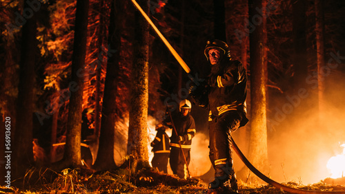 Group of Experienced Firefighters Extinguishing a Wildland Brushfire Deep in the Forest. Professional Fireman Wearing Safety Uniform, Spraying Water from Fire Hose to Fight Dangerous Wildfire.