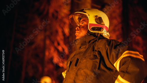 Brave Handsome Young African American Firefighter in Safety Uniform and a Helmet Looking Around the Forest During a Wildfire. Professional Squad Leader Assessing the Dangerous Ecological Situation.