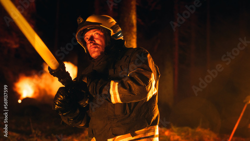 Portrait of a Brave Professional Firefighter Using a Firehose to Fight a Raging Dangerous Forest Fire. Experienced Fireman Skillfully Manages the High-Pressure Water and Stays Safe. Low Angle Shot.