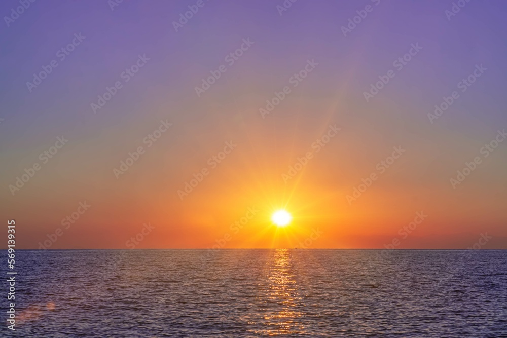 Sunset or sunrise over the sea with blue sky and clouds reflected in the water