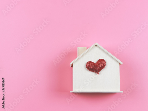 flat lay of wooden model house with red glitter heart on pink background. dream house , home of love, strong relationship, valentines.