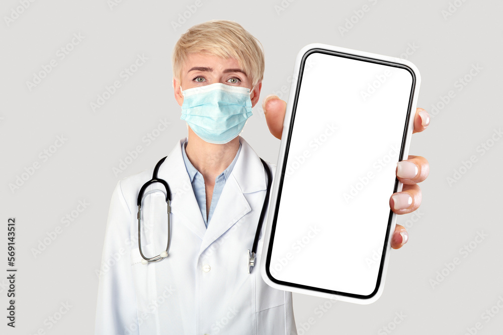 Female doctor in white coat and protective mask showing blank smartphone Female doctor in white coat and protective mask showing blank smartphone