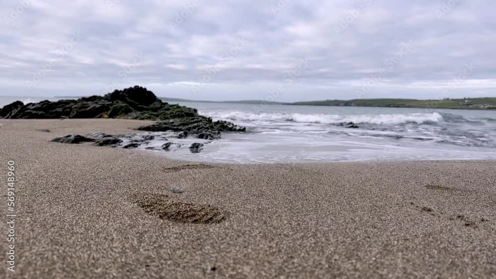 Footsteps in the sand and black shiny rocks with gentle waves washing the shore in slow motion. Footsteps in the sand and black shiny rocks with gentle waves washing the shore in slow motion.