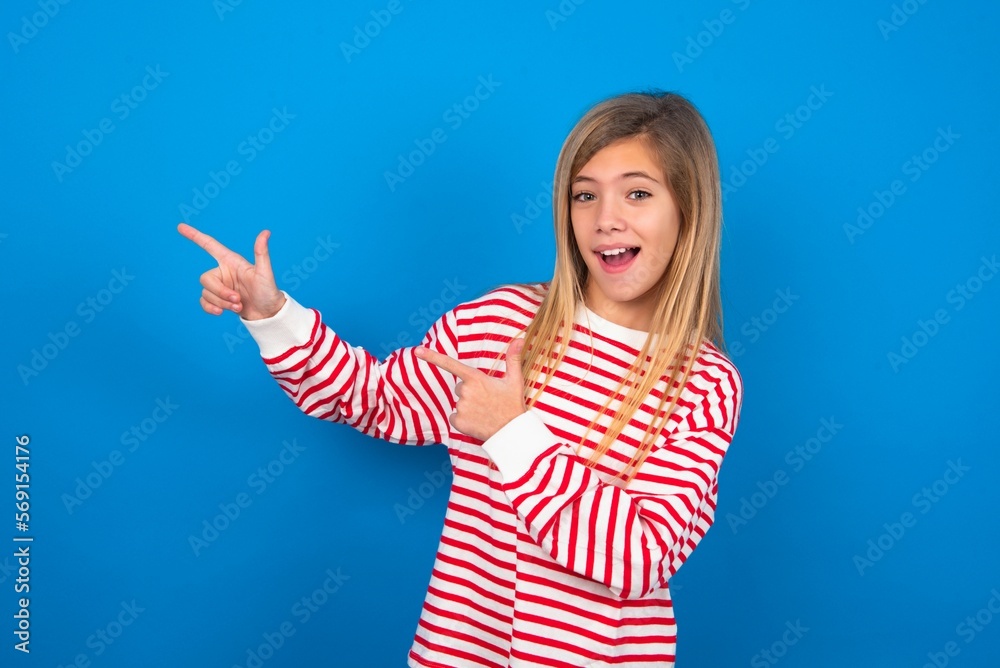 caucasian teenager girl wearing striped T-shirt over blue background point at copyspace recommend sales discounts caucasian teenager girl wearing striped T-shirt over blue background point at copyspace recommend sales discounts