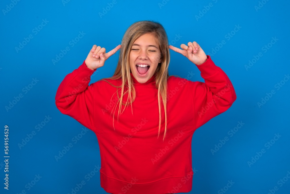 Fototapeta premium Photo of crazy caucasian teenager girl wearing red sweater over blue background screaming and pointing with fingers at hair closed eyes