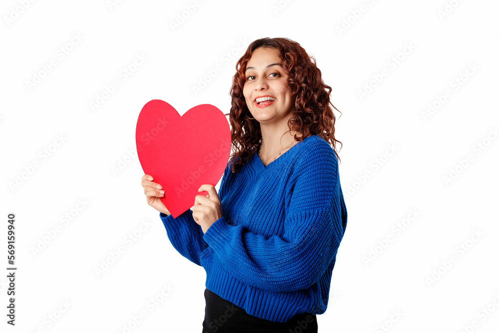 Cute millennial woman wearing pullover sweater standing isolated over white background thinking about lover and laughs while holding a large cardboard heart shape. Cute millennial woman wearing pullover sweater standing isolated over white background thinking about lover and laughs while holding a large cardboard heart shape.
