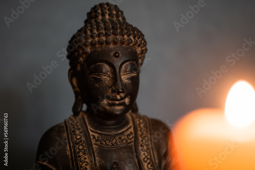 Statue of Buddha with selective focus and blurred candlelight in the foreground. Buddhism concept