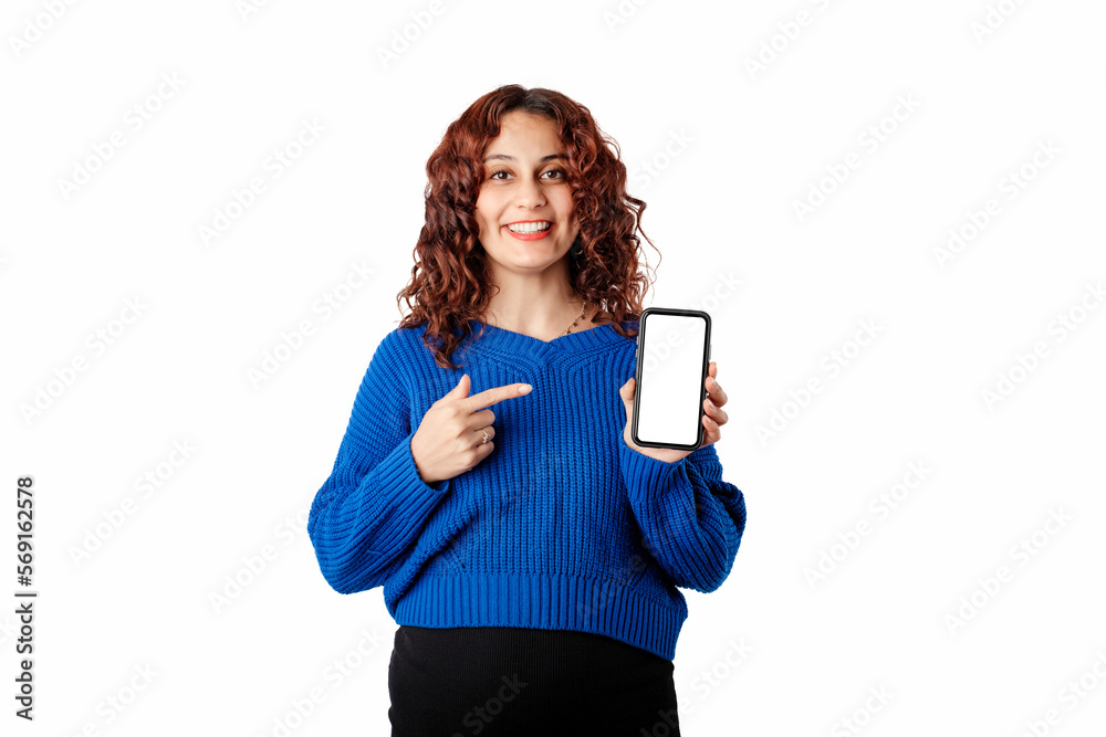 Portrait of young woman wearing blue pullover sweater isolated over white background holds the phone with hand and points with index finger to the empty white blank mockup screen. Portrait of young woman wearing blue pullover sweater isolated over white background holds the phone with hand and points with index finger to the empty white blank mockup screen.