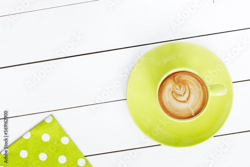 cappuccino coffee in green cup,   with napkin at polka dots scattered on white painted wooden table, top view