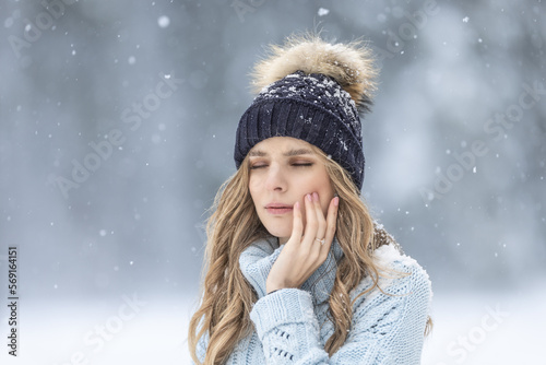 A young woman has a toothache outside in winter weather, she has sensitive enamel to the cold