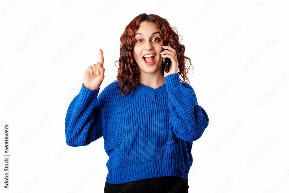 Cheerful woman wearing blue sweater isolated over white background having an idea or question while talking on mobile phone pointing finger up. Gets very excited and looks at the camera. Number one. Cheerful woman wearing blue sweater isolated over white background having an idea or question while talking on mobile phone pointing finger up. Gets very excited and looks at the camera. Number one.
