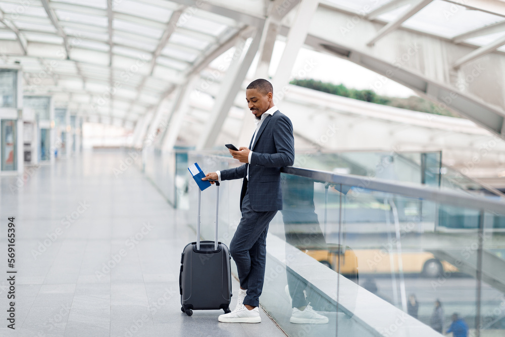 Fototapeta premium Smiling Black Businessman Messaging On Smartphone While Waiting Flight At Airport