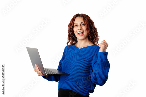 Happy woman wearing pullover sweater standing isolated over white background celebrating online win, great deal or business success holding laptop. Makes a winning gesture, happy to win the prize.