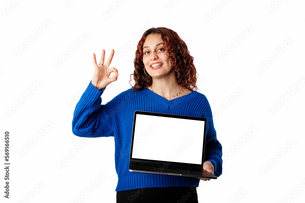 Portrait of woman wearing blue knitted sweater standing isolated over white background holding a laptop with a blank white mockup screen, smiles at the camera doing okay sign with hand. Portrait of woman wearing blue knitted sweater standing isolated over white background holding a laptop with a blank white mockup screen, smiles at the camera doing okay sign with hand.