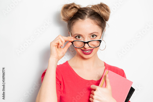 Fototapeta Naklejka Na Ścianę i Meble -  the portrait of young blondie caucasian woman with two hair bundles, glasses for vision, braces smiling widely and holding some notebooks; young woman businessman concept 